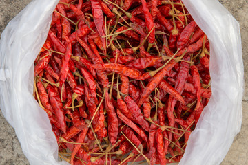 Dried chillies in white plastic bags placed on concrete floor