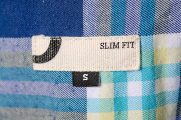 Size S textile clothes label tag slim fit on cage blue yellow white cotton background