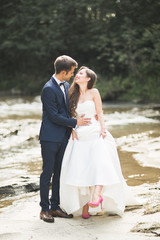 Naklejka premium Beautifull wedding couple kissing and embracing near the shore of a mountain river with stones