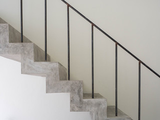 Closeup of raw concrete staircase with black railing on the white wall