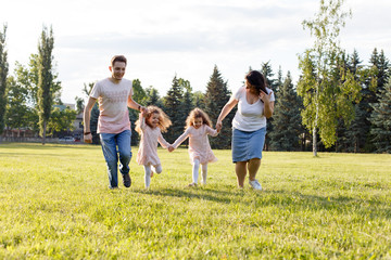 Fototapeta premium Smiling Family Running Across Summer Field Together, happy family with twin toddler girls