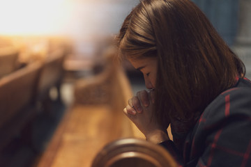 A Christian girl is sitting and praying with broken heart in the church.