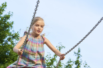  Little child blond girl having fun on a swing outdoor. Summer playground. Girl swinging high. Young child on swing outdoors.