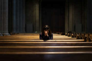 A Christian girl is sitting and praying with broken heart in the church.