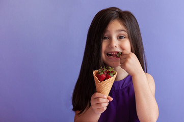 Cute little child girl eating fresh strawberries from ice cream horn. Healthy food. Summer time.