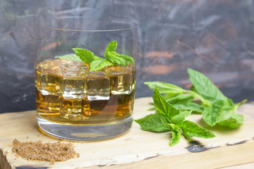 Glass of rum with ice and mint on wood.