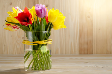Bunch of Colorful tulip flowers in glass vase on wooden table background with space for text