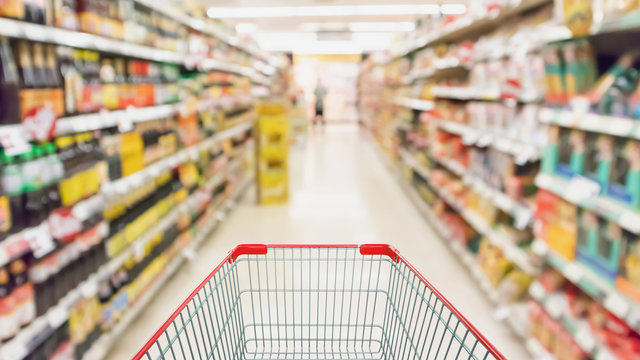 Empty shopping cart with supermarket shelves aisle interior blur defocused background