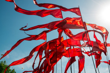 Scarlet flags in the wind against the blue sky in the sun.