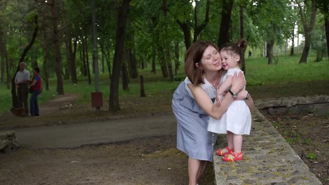 Mom kisses her baby girl in a green park