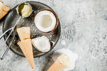 Summer healthy dessert, organic vegan coconut ice cream served in halves of coconut and ice cream cones, gray concrete background