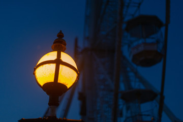 Fototapeta na wymiar atmospheric image of old fashioned vintage yellow lantern with big ferris wheel in background at night
