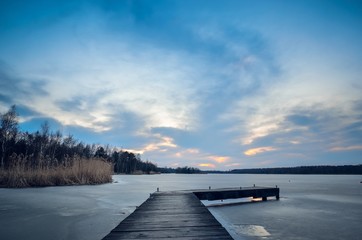 Fototapeta premium Evening winter landscape. Wooden pier over a beautiful frozen lake.