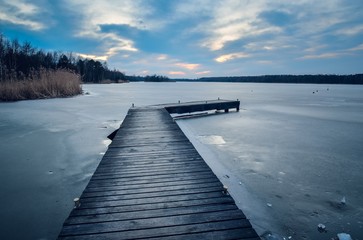 Evening winter landscape. Wooden pier over a beautiful frozen lake.