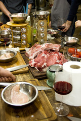 there are pieces of raw meat for steak on a wooden table  background with people hands and iron plates with tomatoes on the kitchen