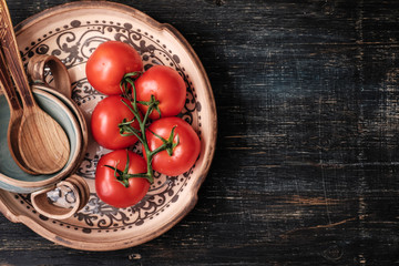 Tomatoes on a branch on the beautiful patterned old dish on an old wooden background