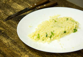 plate with couscous  on wooden background with knife and fork