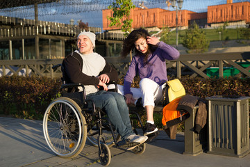 Happy couple - disabled man in wheelchair talking with attractive young woman enjoing the sunset