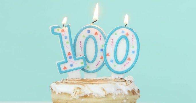 Birthday cake with burning candles as number one hundred 100 on pastel blue background
