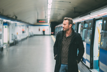 Happy young blonde man with backpacking inside the underground station waiting for the train