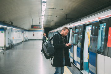 Happy young blonde man with backpacking inside the underground station waiting for the train