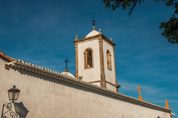 Fototapeta premium Overview of lamp, wall and old belfry under blue sunny sky in Paraty, an amazing and historic town totally preserved in the coast of the Rio de Janeiro State, southwestern Brazil