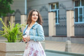 Fototapeta premium beautiful brunette girl in a jeans jacket walks around the city with coffee in hands