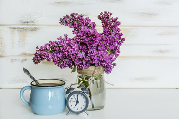 Bouquet of Lilac with Alarm Clock and Cup of Coffee on  Wooden Background .Spring Morning Concept