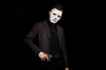 A man in a white mask on a black background, pulls a pistol from his pocket