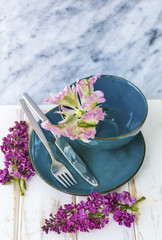 Spring Table Setting with Vintage Blue Cutlery , Lilac Flowers and Pink Tulip  on a Marble Background.Floral Table Decor