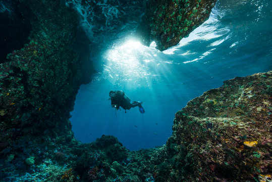 Woman Diver Underwater At The Entrance Of A Cave With Sunrays