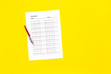 Exam sheet on yellow table flat lay copy space. Education concept