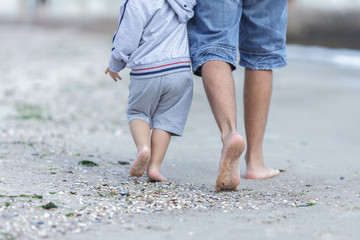 the feet of dad and child going for a walk on a coast