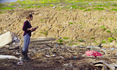 Woman ecologist during the research on garbage dump. She writing something on the sheets of paper.