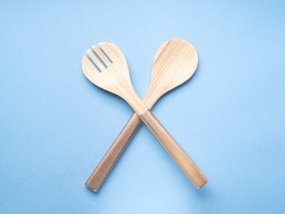 Minimal cooking, eating concept on blue background with wooden salad fork and spoon.