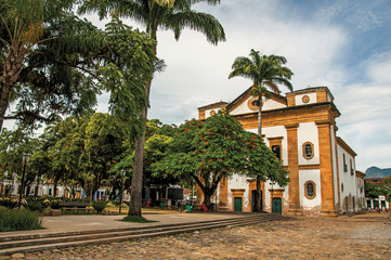 Overview of old colored church, garden with trees and cobblestone street in Paraty, an amazing and historic town totally preserved in the coast of the Rio de Janeiro State, southwestern Brazil