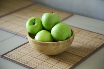 green fresh apples are in a wooden bowl in the kitchen