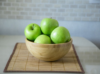 green fresh apples are in a wooden bowl in the kitchen
