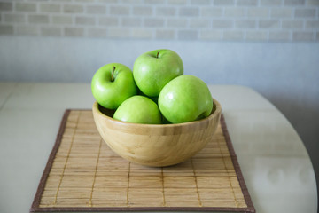 green fresh apples are in a wooden bowl in the kitchen