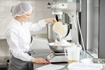 Woman confectioner in uniform weighing ingredients for pastry working at the bakery manufacturing