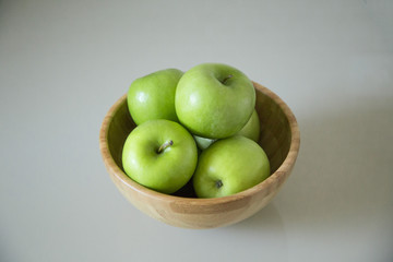 green fresh apples are in a wooden bowl in the kitchen