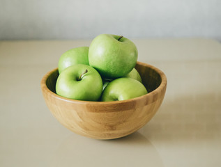 green fresh apples are in a wooden bowl in the kitchen