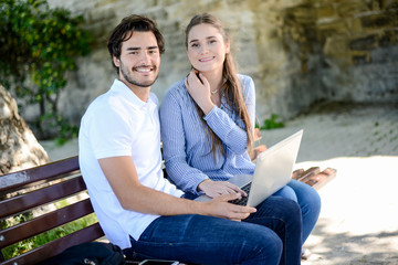 couple of young students man and woman working together with a laptop computer outdoor in a street during summer