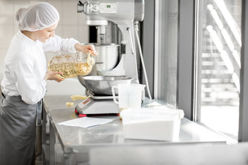 Woman confectioner in uniform weighing ingredients for pastry working at the bakery manufacturing