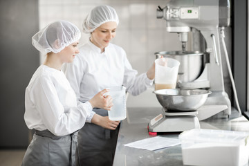 Two female confectioners in uniform weighing ingredients for pastry working at the bakery...