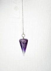 Purple Amethyst crystal pendulum on chain on white background.