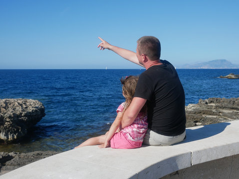 Father with his little daughter sitting on a sea cost (Favignana, Sicily, Italy).