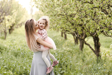 Obraz premium Mother kissing baby girl 2-3 year old in park over green nature background. Motherhood. Maternity.