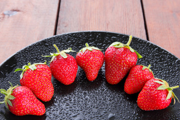 Strawberries on a black plate top view, red berries on a wooden background, fresh strawberries on dark wooden boards, vegetarian food