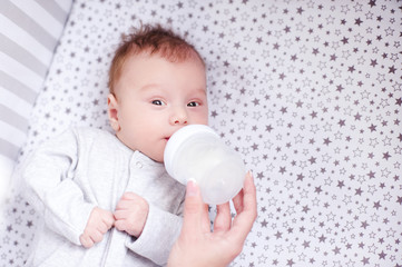 Mother feeding baby boy with milk in bed. Healthy nutrition.